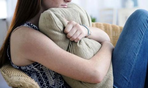 Image of a young adult clutching a sofa pillow during counseling. 